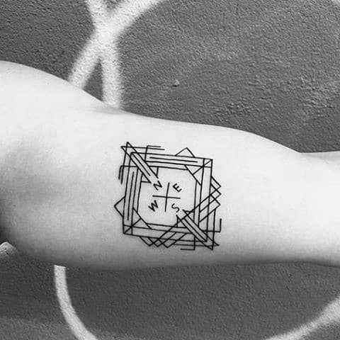 Minimalist compass tattoo on arm featuring layered squares and bold directional letters in a clean, geometric style.