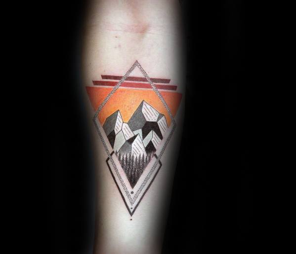 Geometric forearm tattoo of abstract mountains and trees framed in a diamond shape with bold orange and red sunset tones.