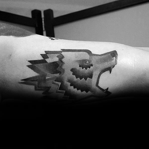 Geometric wolf head tattoo in black and grey gradient with sharp, jagged edges and a bold, stylized expression on the inner arm.
