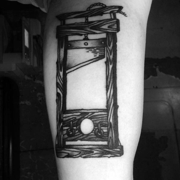 Bold blackwork guillotine tattoo with heavy woodgrain texture, dark shading on the blade, and clean lines for a striking visual impact.