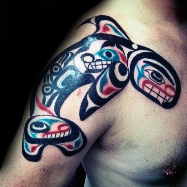 Bold tribal-style orca tattoo on the shoulder, featuring dynamic shapes with black, red, and blue accents that create a vibrant and flowing design.