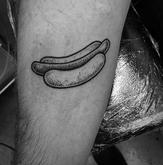 Tattoo of two simple, line-drawn hot dogs on the forearm, done in black ink with a dotted texture.