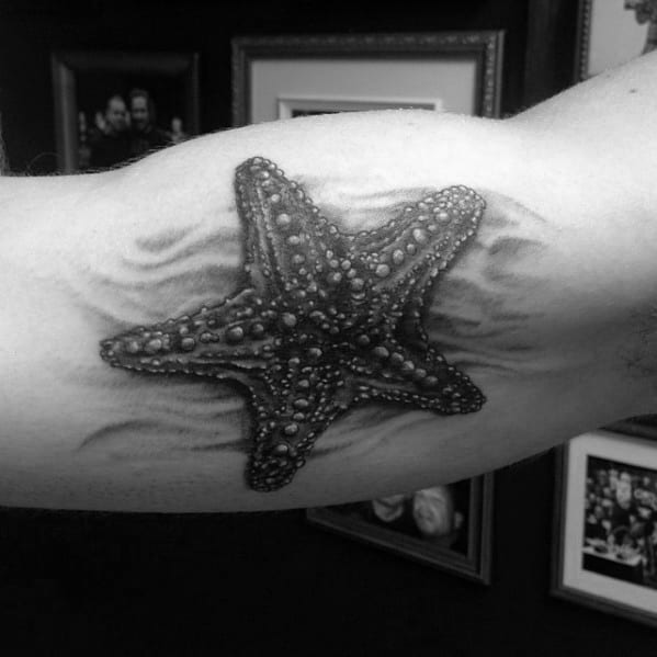 Realistic black and grey starfish tattoo on the inner bicep, with textured detail and soft shading resembling sand ripples.