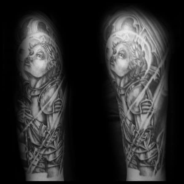 Black and grey Joan of Arc tattoo sleeve with a glowing halo, upward gaze, and intricate armor design, radiating divine strength and hope.