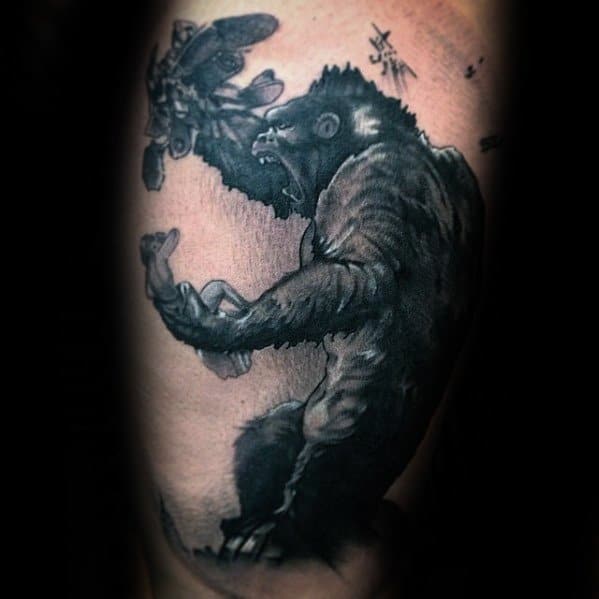 Black and grey King Kong tattoo showing Kong mid-roar as he swats at biplanes in the sky, with dynamic shading and dramatic motion.