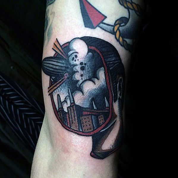 Neo-traditional tattoo of a Zeppelin airship exploding over a cityscape, framed within a bold black and red design shaped like a helmet or head.