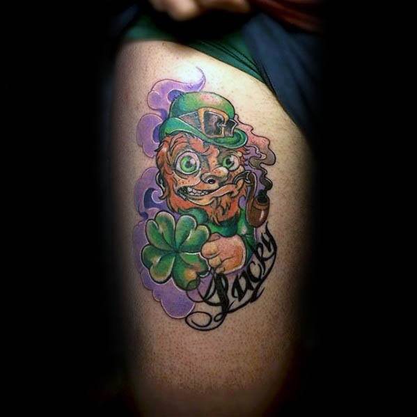 Colorful tattoo of a wide-eyed leprechaun holding a large four-leaf clover and smoking a pipe, with purple smoke and the word "Lucky" below.