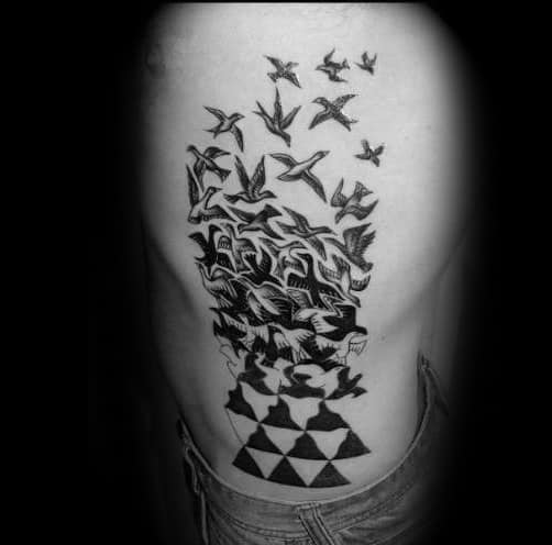 MC Escher-inspired rib tattoo of birds emerging from geometric shapes, transforming from structured patterns into free-flying forms.