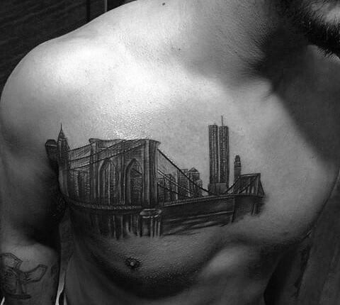 Black and gray chest tattoo of the Brooklyn Bridge with the New York City skyline in the background, including the Twin Towers.