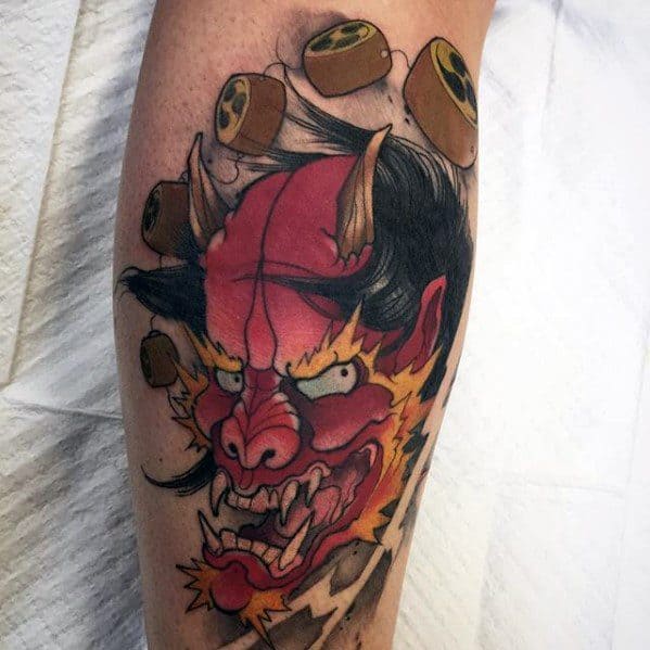 Raijin calf tattoo with intense red demon face, sharp fangs, blazing lightning aura, and floating tomoe drums in bold style.