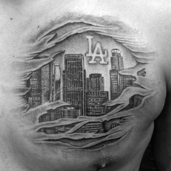 Chest tattoo of Los Angeles skyline with realistic torn-skin effect revealing buildings and bold "LA" logo in black and gray ink.