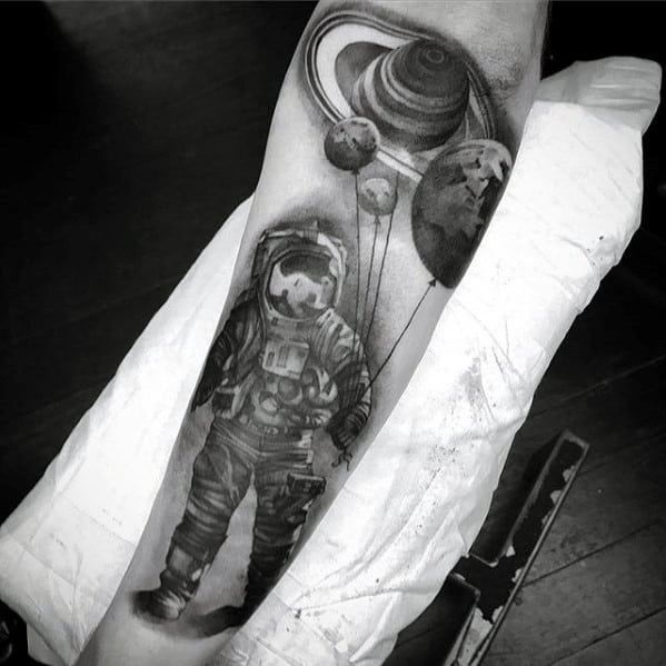Realistic Saturn tattoo design for men featuring an astronaut holding planet-shaped balloons with Saturn towering above in a detailed space scene.