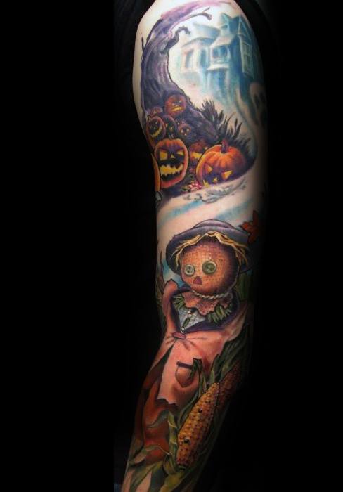 Colorful full sleeve tattoo featuring a cute scarecrow with button eyes, corn stalks, jack-o'-lanterns, and a haunted house in a spooky landscape.