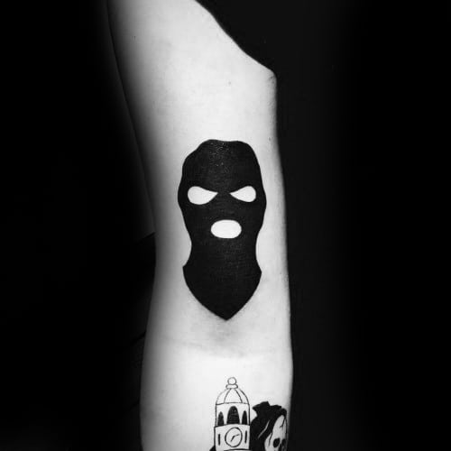 Bold black ski mask tattoo with cutouts for eyes and mouth, placed on the back of the arm for a striking silhouette effect.
