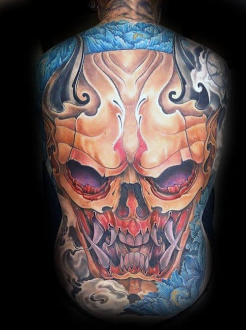Vibrant full-back tattoo of a demonic skull with fiery red eyes and sharp fangs, surrounded by swirling blue and gray smoke.