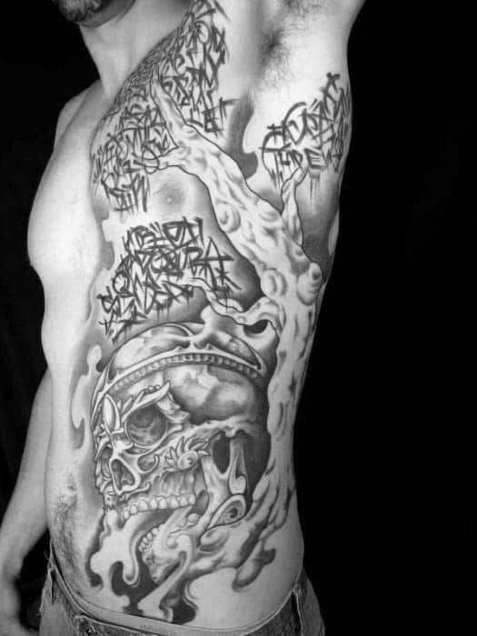 Large side tattoo featuring a twisted tree, graffiti-style text in the branches, and a detailed skull surrounded by smoke and abstract shapes.