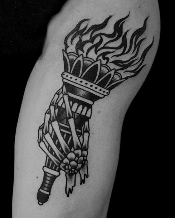 Bold blackwork torch tattoo with intense flames, held by a skeletal hand wrapped in tattered bandages and detailed linework.