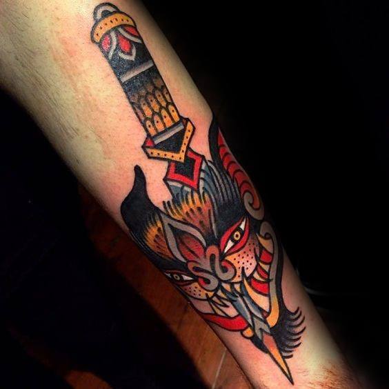 Traditional tattoo of a dagger piercing a fierce bat head with red, orange, and black tones, bold lines, and decorative detailing.