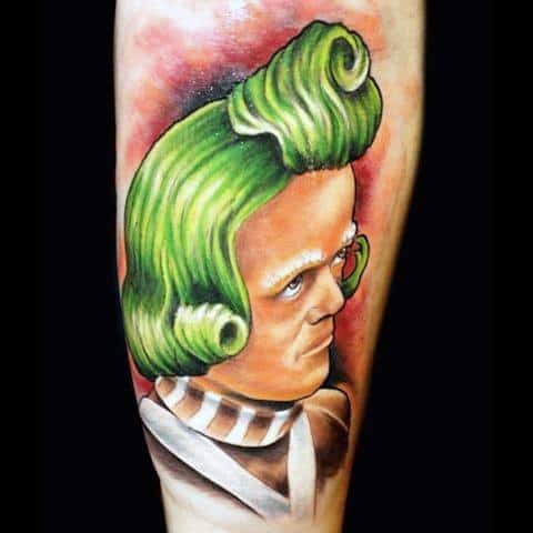 Bold Oompa Loompa tattoo with vivid green hair, white eyebrows, and a brown-and-white uniform set against a red-pink gradient background.