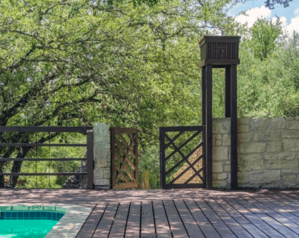 Wooden deck with a pool, gate, and tall structure amid lush greenery
