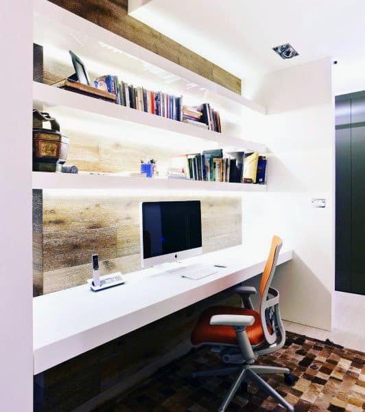 Compact home office with white desk, illuminated shelves, and ergonomic orange chair.