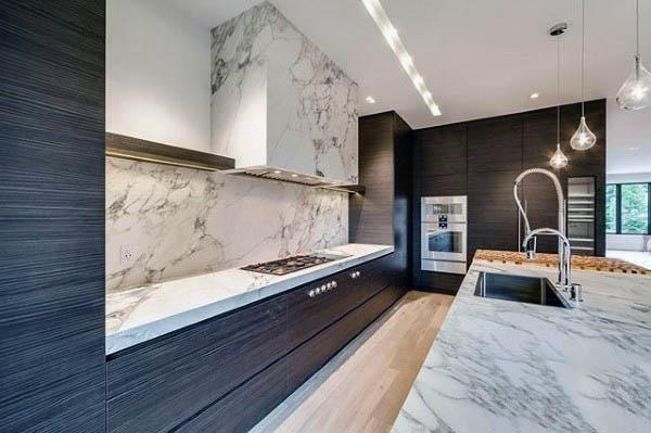 Sleek kitchen with black cabinets, marble countertops, backsplash, and pendant lighting.