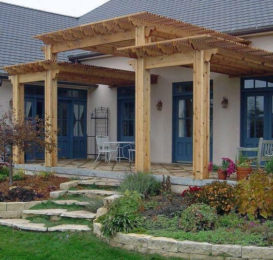 Wooden pergola with natural beams over a patio featuring blue French doors and garden steps.