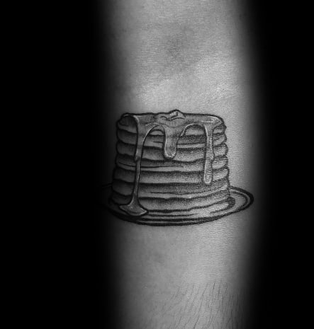 Black and grey pancake tattoo featuring a stacked pile with dripping syrup and butter on a plate, shaded for a simple yet realistic look.
