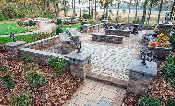 A landscaped patio with stone pathways, benches, and seating, surrounded by trees and lush greenery
