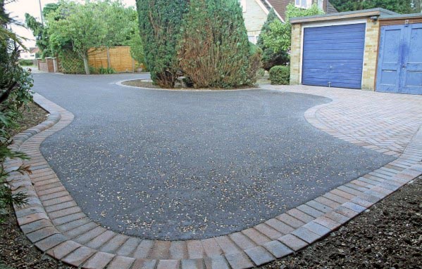 Asphalt driveway with curved brick edging leading to a blue garage and landscaped yard.