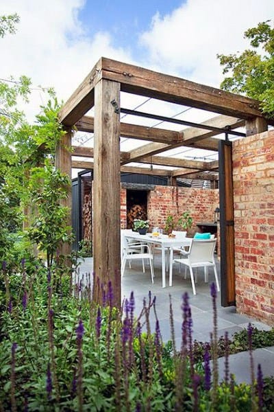Rustic pergola with wooden beams, brick walls, glass roof, and white outdoor dining set.