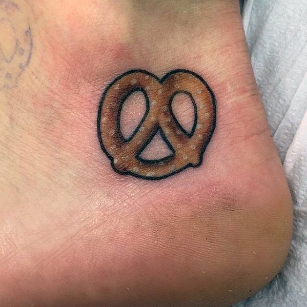 Small realistic pretzel tattoo on the foot, featuring subtle shading, a crisp brown hue, and a thin black outline for a simple yet detailed look.