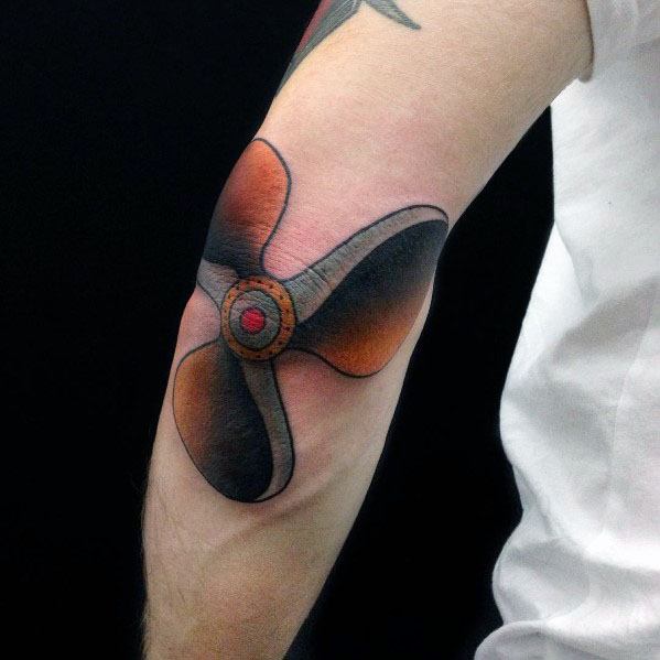 Colorful three-blade propeller tattoo on the elbow with bold shading, black outlines, and red accents for a dynamic mechanical design.
