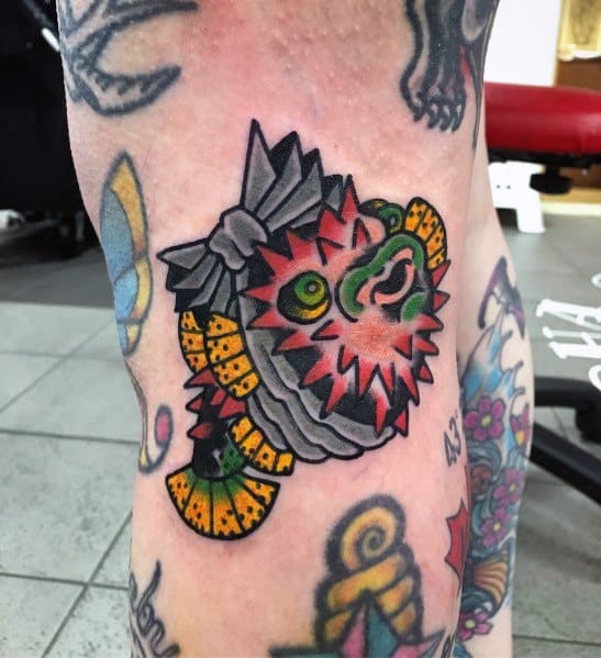 Traditional Japanese-style pufferfish tattoo with bold outlines, vibrant red and yellow hues, and a decorative ribbon, creating a striking design.