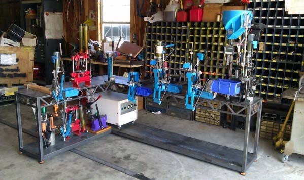 Expansive reloading setup with a robust metal bench featuring multiple presses, a variety of tools, and ample organizational storage for components. The industrial design ensures durability, while the organized grid shelves in the background provide efficient access to supplies.
