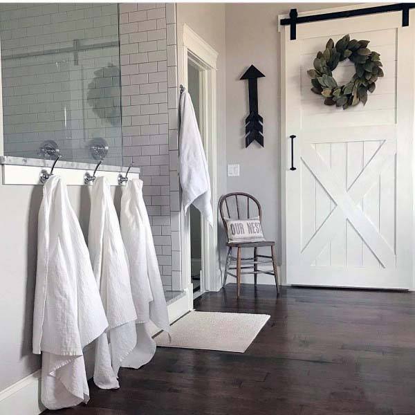 Rustic bathroom with white towels, barn door, wreath; chair holding "Our Nest" pillow