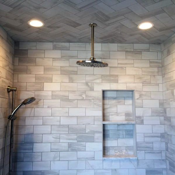Elegant shower with a herringbone-patterned tile wall, a sleek overhead showerhead, and recessed ceiling lights for a bright, modern look