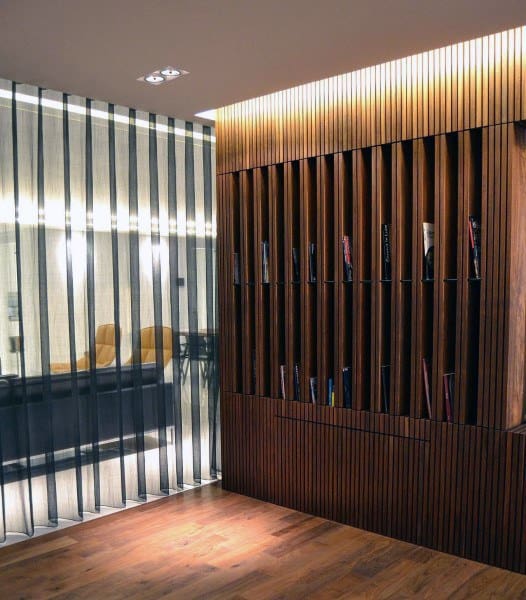 Modern room with vertical wood slat panel, integrated bookshelf, sheer striped curtains, and hardwood floor