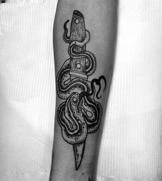 Black ink snake and dagger tattoo on forearm, featuring intricate line work and dot shading for a bold yet detailed traditional design.