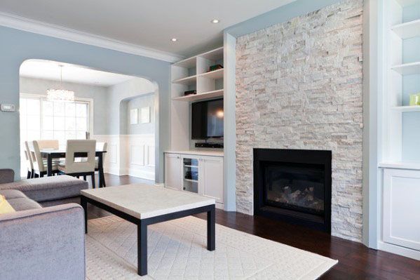 Modern living room with stacked stone fireplace, TV, gray sofa, and dining area in the background