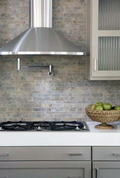 Elegant kitchen with a textured gray stone tile backsplash, modern stainless steel range hood, and soft gray cabinets paired with frosted glass panels for a clean and contemporary look