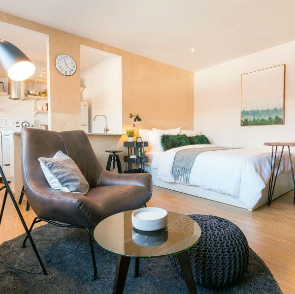 Stylish studio with warm tones, a cozy bed, a leather chair, and chic decor elements.