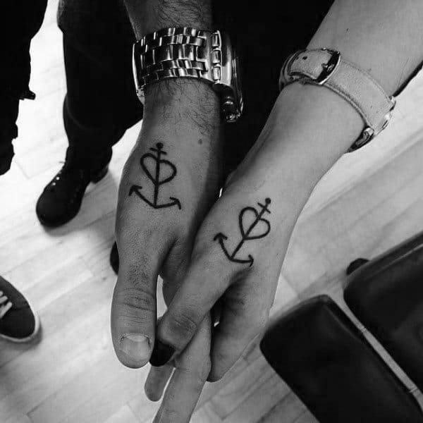 Matching hand tattoos of anchors combined with male and female symbols, representing stability, unity, and a balanced relationship rooted in love.