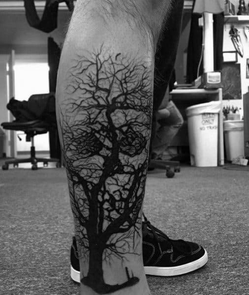 Black ink tree tattoo on the calf, featuring intricate branches and deep shading for a bold, realistic, and nature-inspired design.