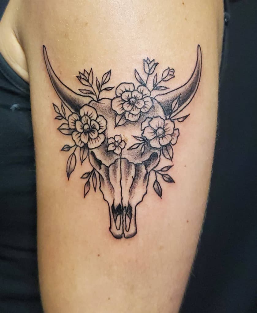 Tattoo of a bull skull with flowers and leaves on an upper arm