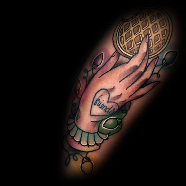 Traditional-style tattoo featuring a hand holding a waffle, a heart tattoo reading "friends," and colorful Christmas lights for a nostalgic design.