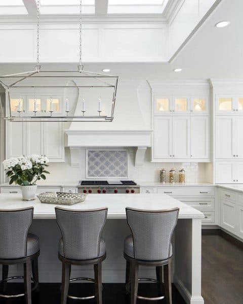 White kitchen with marble island, grey bar stools, and a sleek pendant chandelier.