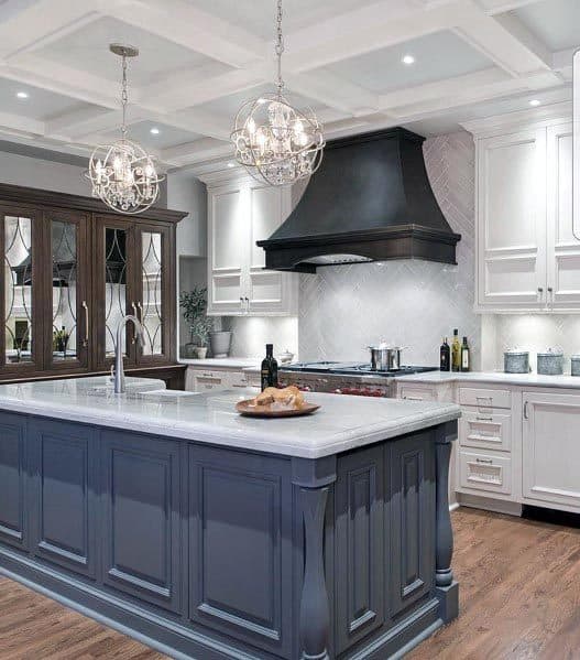 White kitchen with navy island, black range hood, and crystal pendant lighting.