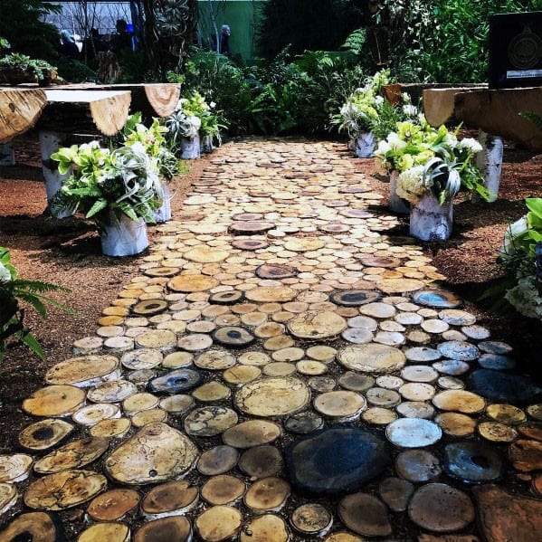 Walkway of circular wood slices lined with white flower arrangements and green foliage