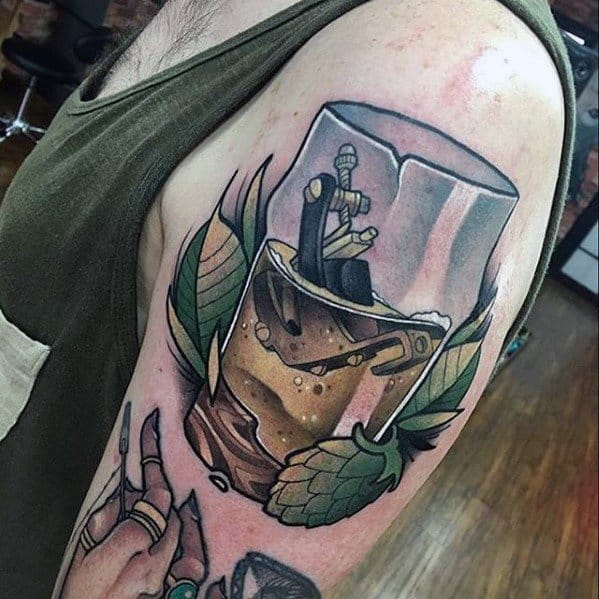 Colorful upper arm tattoo of a beer mug with a sword plunged inside, surrounded by hop cones and leaves, blending medieval fantasy with craft beer imagery.